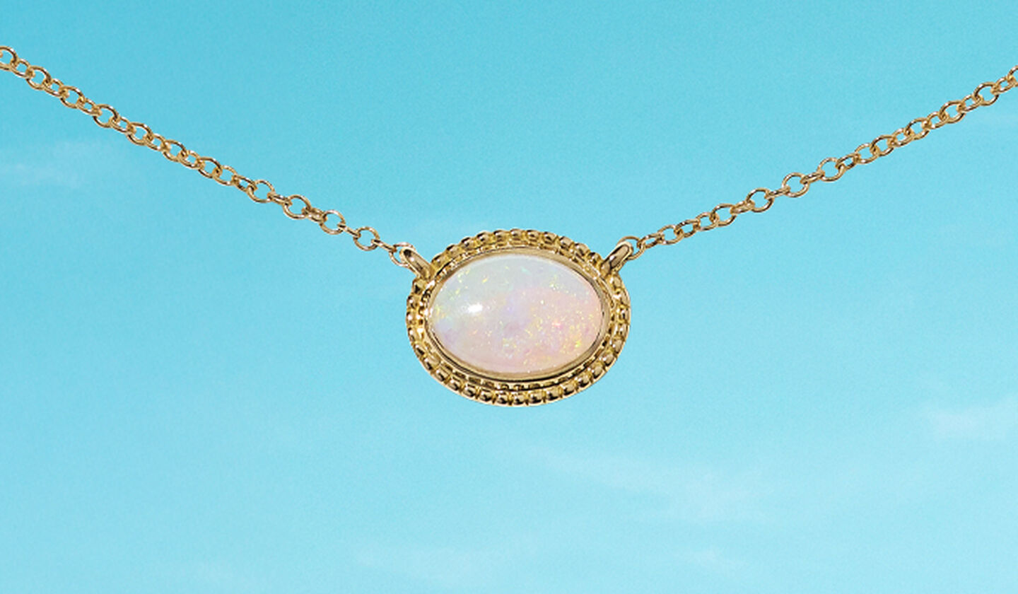 A Birks Essentials yellow gold opal pendant necklace on a blue background.